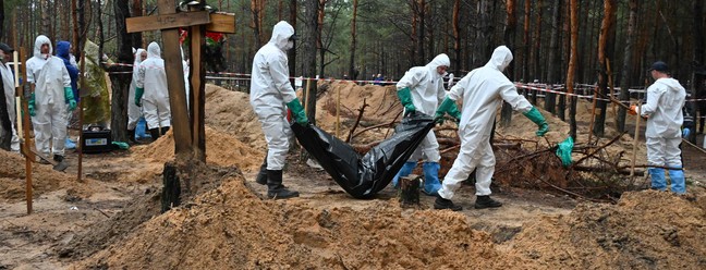 Investigadores carregam um saco de corpos em uma floresta perto de Izium, leste da Ucrânia. — Foto: SERGEY BOBOK / AFP