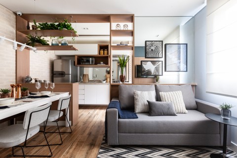 O sofá cinza, feito sob medida por um tapeceiro, combina com a marcenaria planejada branca e madeira. Espelhos, atrás do sofá e na cozinha, aumentam a amplitude do imóvel. Projeto do escritório Dirani e Marchió