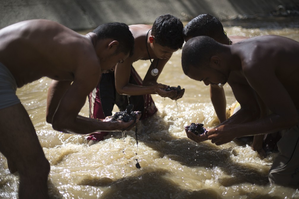 Ángel Villanueva (o mais da direita) e seus companheiros procuram objetos de valor no poluído Rio Guaire (Foto: Ariana Cubillos/AP)