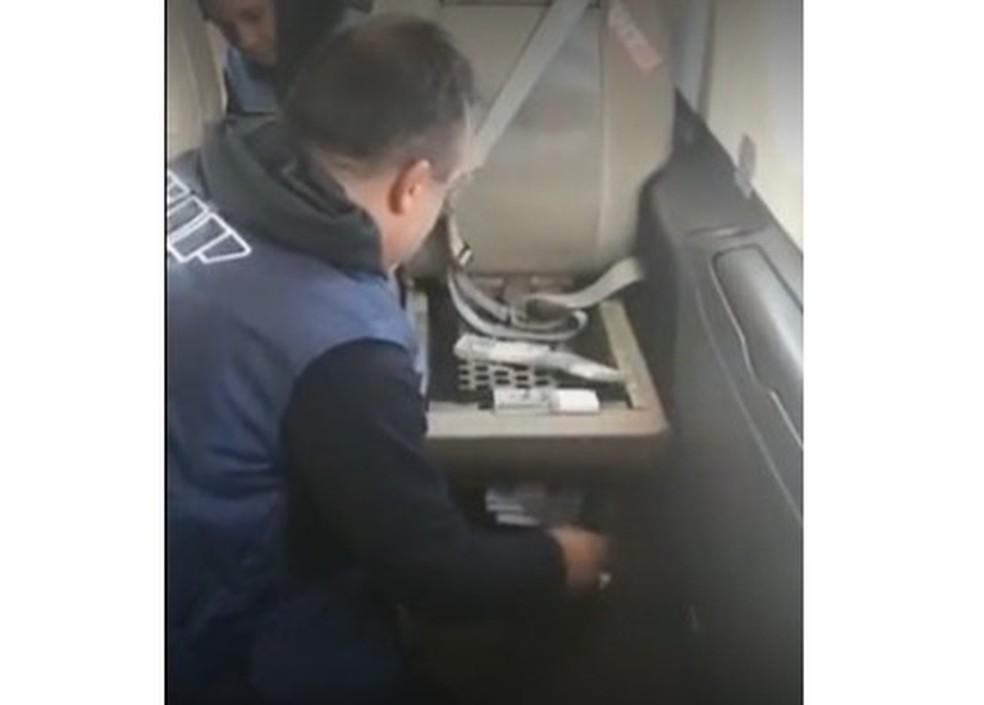 Agente recolhendo notas embaixo do banco da aeronave — Foto: Clarín/Reprodução