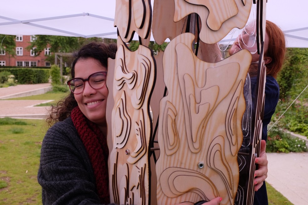 Caroline Gaudeoso, de 27 anos, explica que a "Hugging tree" é um tronco de arvore que vibra, para que dessa forma pessoas surdas possam abraçar a música — Foto: Divulgação