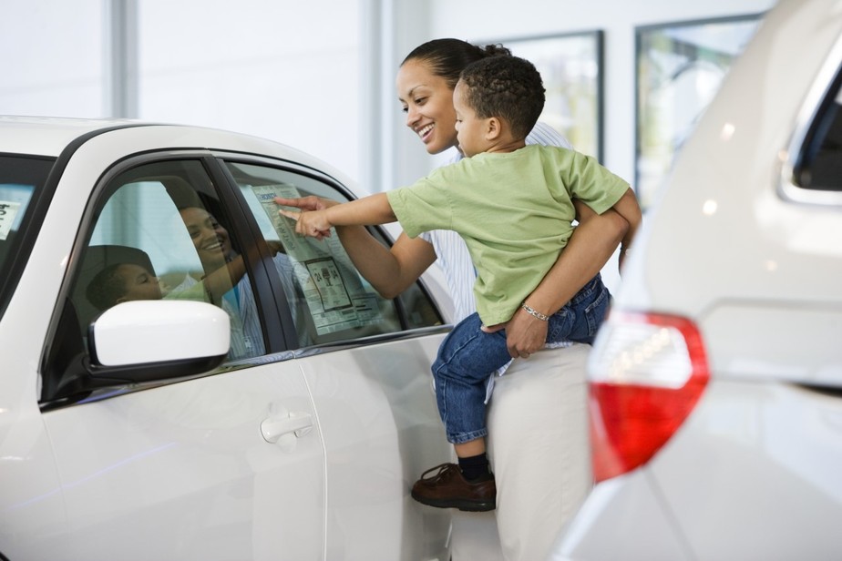 Criança no colo da mãe vendo/escolhendo um carro