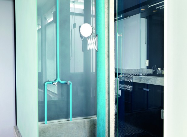 Na área do chuveiro deste banheiro, a tubulação e o cano de esgoto foram pintados de azul. O tom vibrante ganha ainda mais força na presença da estrutura de concreto (Foto: Victor Affaro/Editora Globo)