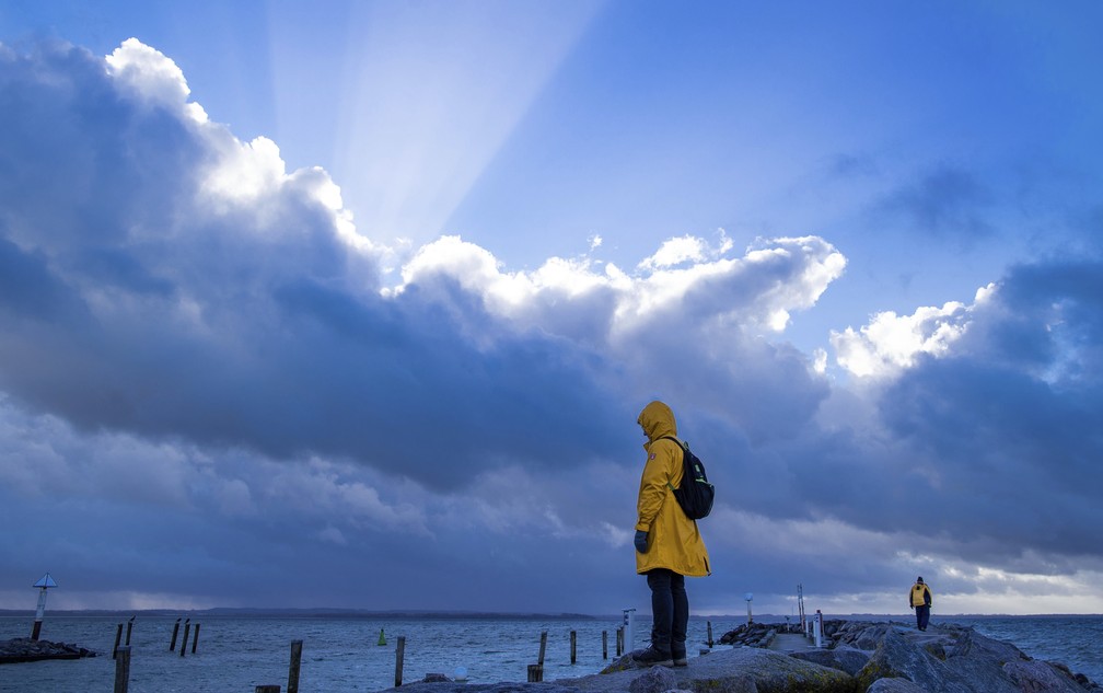 Uma mulher vestindo uma capa de chuva amarela atravessa o cais em um pequeno porto de pesca na ilha de Poel, no Mar Báltico, perto de Timmendorf, na Alemanha, nesta segunda-feira (3)   — Foto: Jens Buettner/dpa via AP