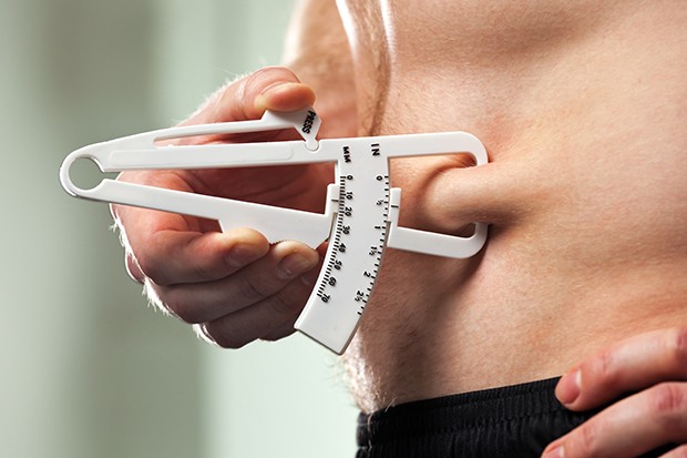 Young man is measuring his body fat with calipers. (Foto: Getty Images/iStockphoto)