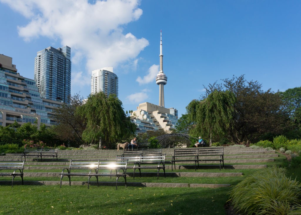 TORONTO, ONTARIO, CANADA - 2017/06/30: Urban skyline including the CN Tower. Point of view from the Music Garden in the Toronto Waterfront. Iron benches shining in bright sun in a public park, they are fixed at short distances and surrounded by trees. (Ph (Foto: LightRocket via Getty Images)