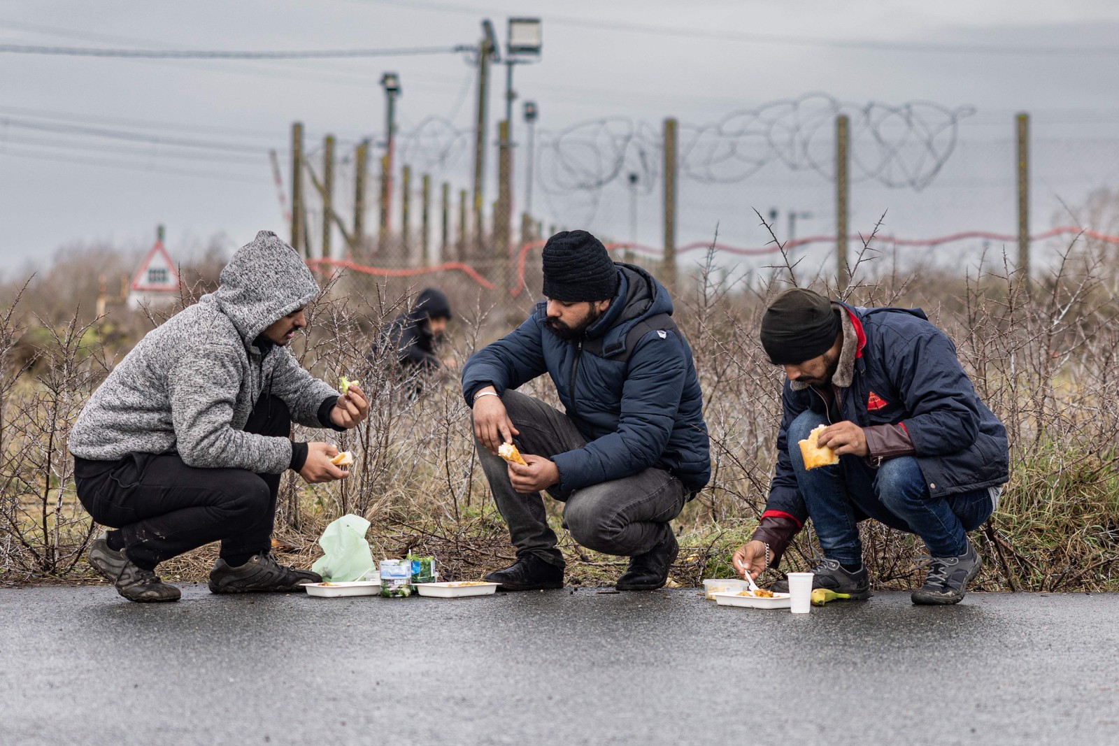 Migrantes comem refeições distribuídas por associações locais em um acampamento improvisado em Mardyck, norte da França — Foto: SAMEER AL-DOUMY/AFP