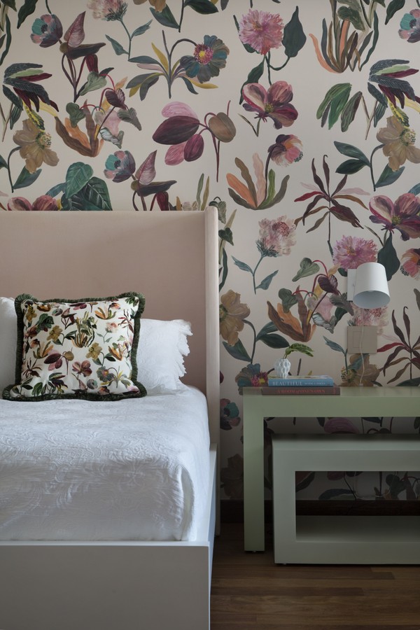detalhe de um dos quartos, com papel de parede floral atrás da cama 