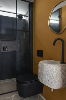 O Studio Julliana Camargo projetou um banheiro cheio de estilo, com ladrilho preto e o tom de amarelo mostarda na parede da pia. Este banheiro também é usado como lavabo