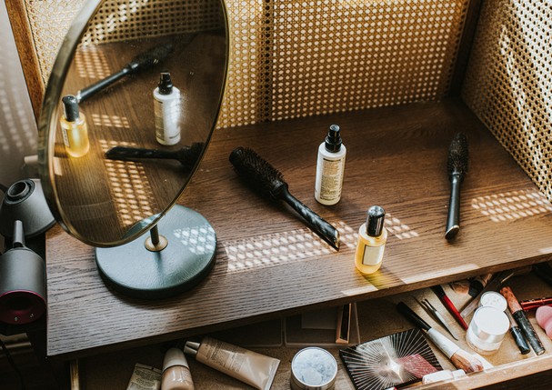 A stylish rattan wooden dressing table in sunlight, with the drawer ajar. Various beauty products are visible within the drawer and on top of the table, including hair oil, leave-in conditioner, foundation, lipstick, make-up palette, and make-up primer. T (Foto: Getty Images)