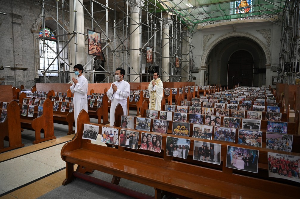 Padre católico Mark de Leon (costas) e os coroinhas caminham pela igreja vazia do Santo Rosário, com fotos de paroquianos em bancos, como parte das medidas de distanciamento social na Filipinas — Foto: Ted Aljibe / AFP Photo