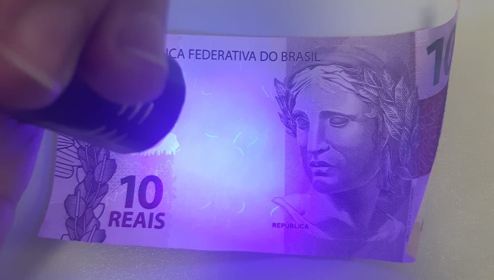 Luz ultravioleta exposta em papel de segurança (dinheiro) é absorvida — Foto: Divulgação