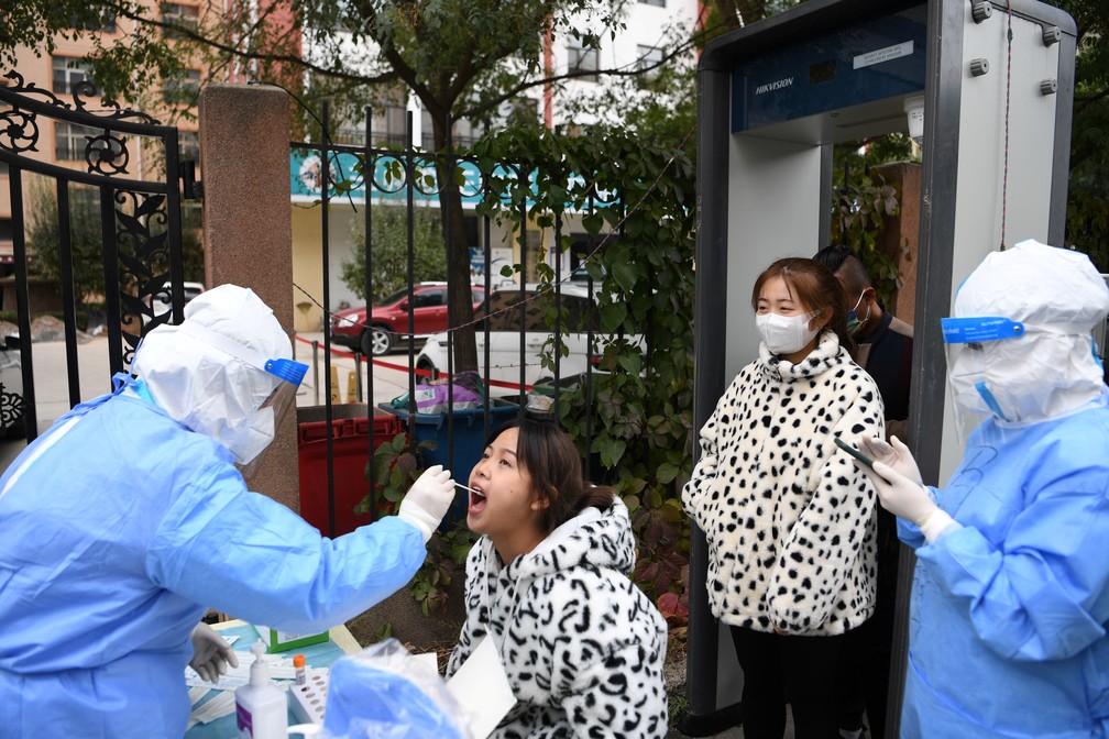 Profissional de saúde com traje de proteção coleta amostra de uma moradora de Lanzhou para um teste de Covid-19  no distrito de Chengguan, na província de Gansu, em 20 de outubro de 2021 na China — Foto: cnsphoto via Reuters