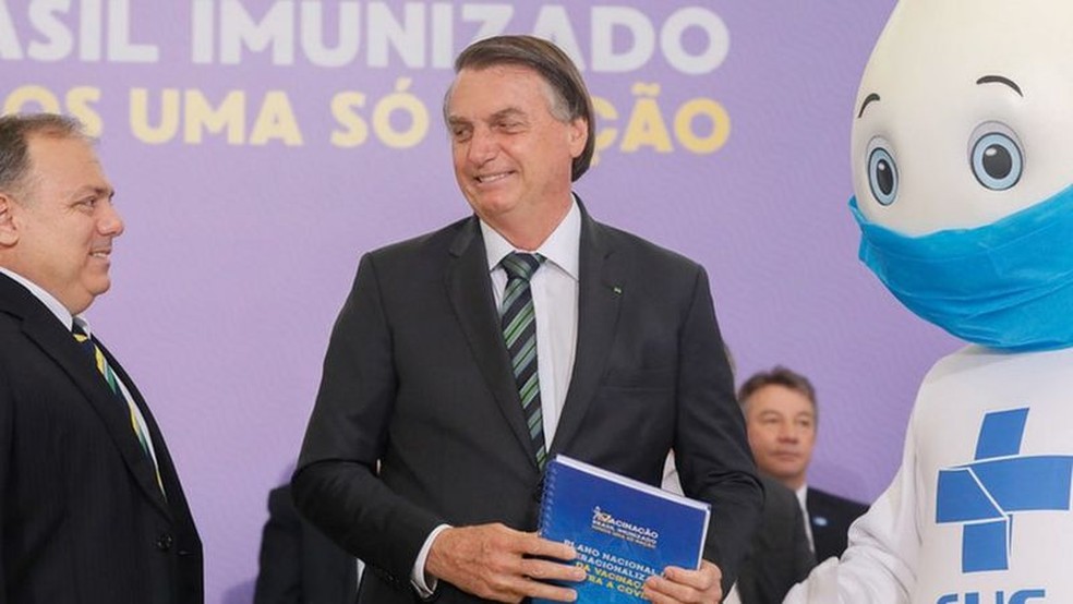 Bolsonaro (ao centro) recebe do ministro da Saúde, Eduardo Pazuello (à esquerda), e do personagem Zé Gotinha (à direita) o Plano Nacional de Operacionalização da Vacinação contra a covid-19 em evento no dia 16 de dezembro de 2020 — Foto: Isac Nóbrega/PR