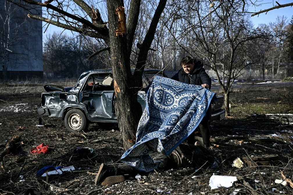 Na cidade de Chuguiv, na Ucrânia, um homem usa um tapete para cobrir o corpo de uma vítima de bombas russas, em 24 de fevereiro de 2022 — Foto: Aris Messinis / AFP