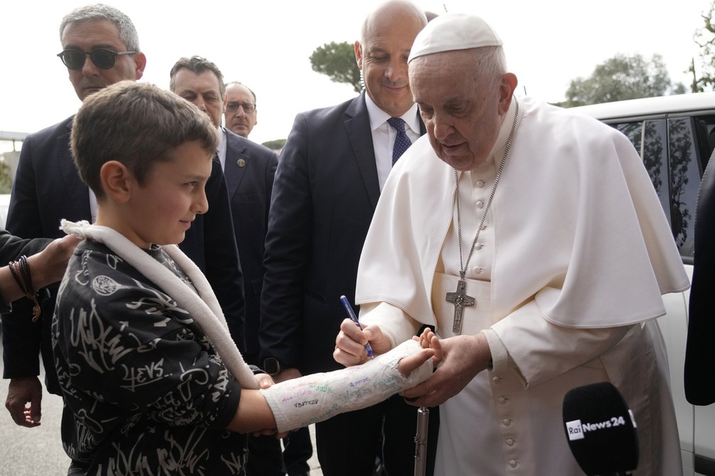Papa Francisco escreve no gesso de um menino ao deixar o hospital no qual esteve internado em Roma para tratar bronquite infecciosa, em 1º de abril de 2023.  — Foto: Gregorio Borga/ AP