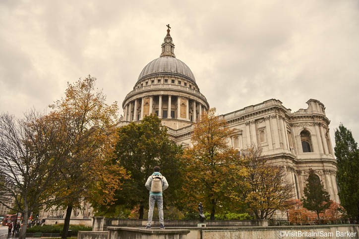 Young man standing on low stone wall and looking up at St Pauls Cathedral, City of London, UK. (Foto: VisitBritain/Sam Barker)
