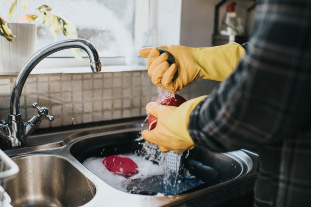 Man standing at the sink, wearing yellow marigold gloves, washing the dishes. (Foto: Getty Images)