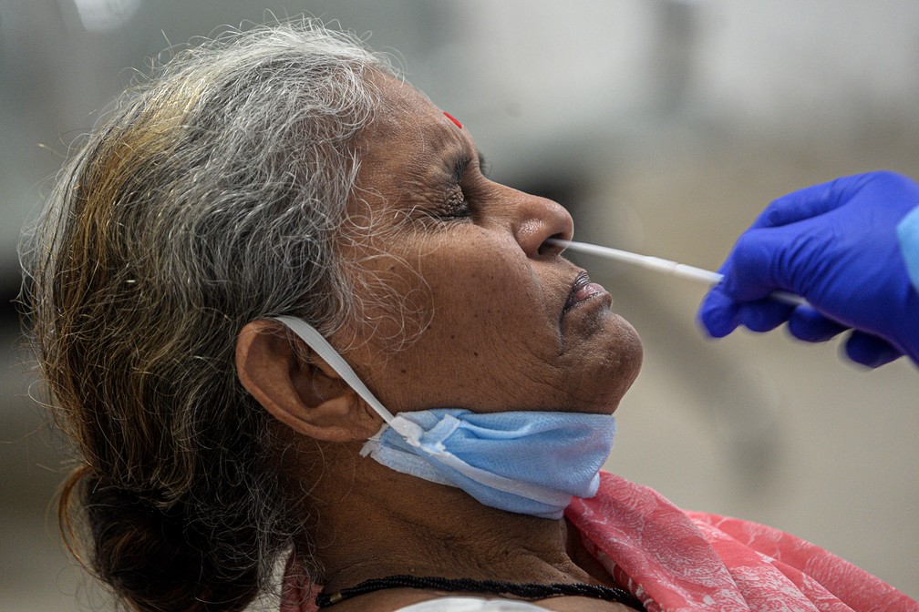 Mulher se retrai enquanto tem amostra do nariz recolhida para teste de Covid-19 em Mumbai, na Índia, nesta segunda-feira (27). — Foto: Indranil Mukherjee / AFP
