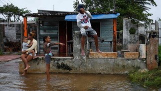 Família é vista fora de sua casa inundada em Batabano, Cuba. A tempestade provocou evacuações em massa e teme-se uma destruição generalizada enquanto se dirige para o estado americano da Flórida — Foto: YAMIL LAGE / AFP