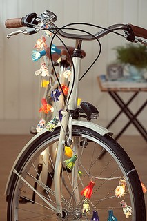 Feitas de feltro, com uma “franja” recortada, as florzinhas envolvem as lâmpadas e transformam até a bike em item de decoração. Bicicleta Trousseau