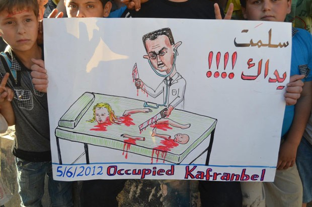 Crianças seguram cartaz com desenho do presidente sírio Bashar al-Assad cortando um corpo e onde se lê em árabe "Muito obrigado", durante protesto na cidade de Kfar Nubul (Foto: AFP)