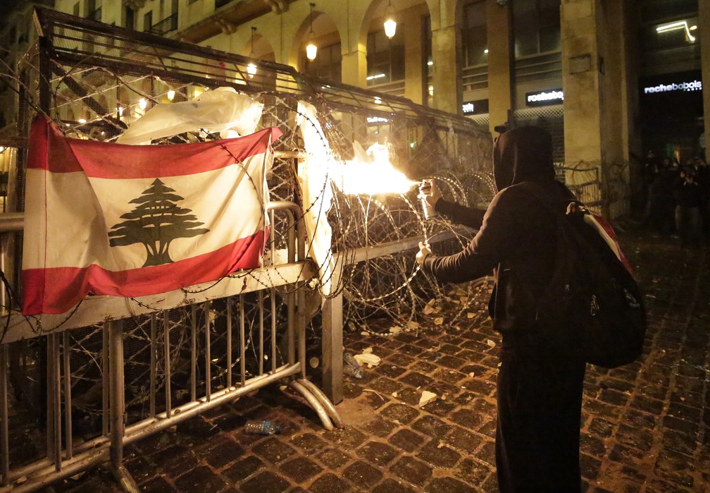 Manifestante lança chamas a partir de spray contra policiais que cercam o Parlamento do Líbano, em Beirute, neste domingo (19) — Foto: Hassan Ammar/AP Photo