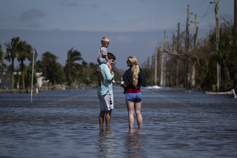 Casal e filho observam área alagada após a passagem do furacão Ian em Fort Myers, na Flórida — Foto: Ricardo Arduengo/AFP