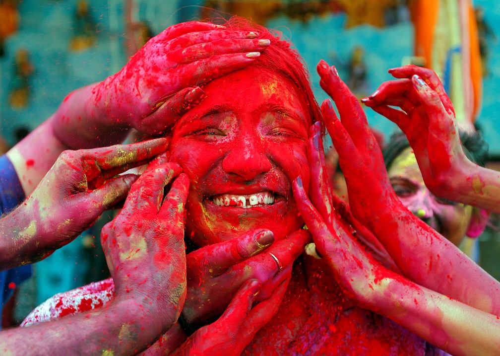 21 de março - Mulher sorri ao ter o rosto coberto com pó vermelho por amigos durante celebração do festival Holi em frente a um templo hindu perto de Calcutá, na Índia — Foto: Rupak De Chowdhuri/Reuters