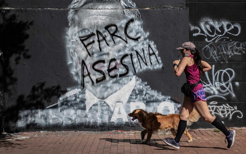 Mulher passa por mural contra as FARC e o ex-presidente colombiano (2002-2010) Álvaro Uribe — Foto: Juan Barreto / AFP Photo