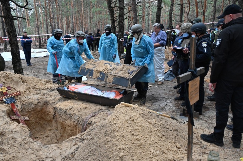 Agentes forenses cuidando de corpos em vala comum na cidade de Izium, na Ucrânia — Foto: SERGEY BOBOK / AFP