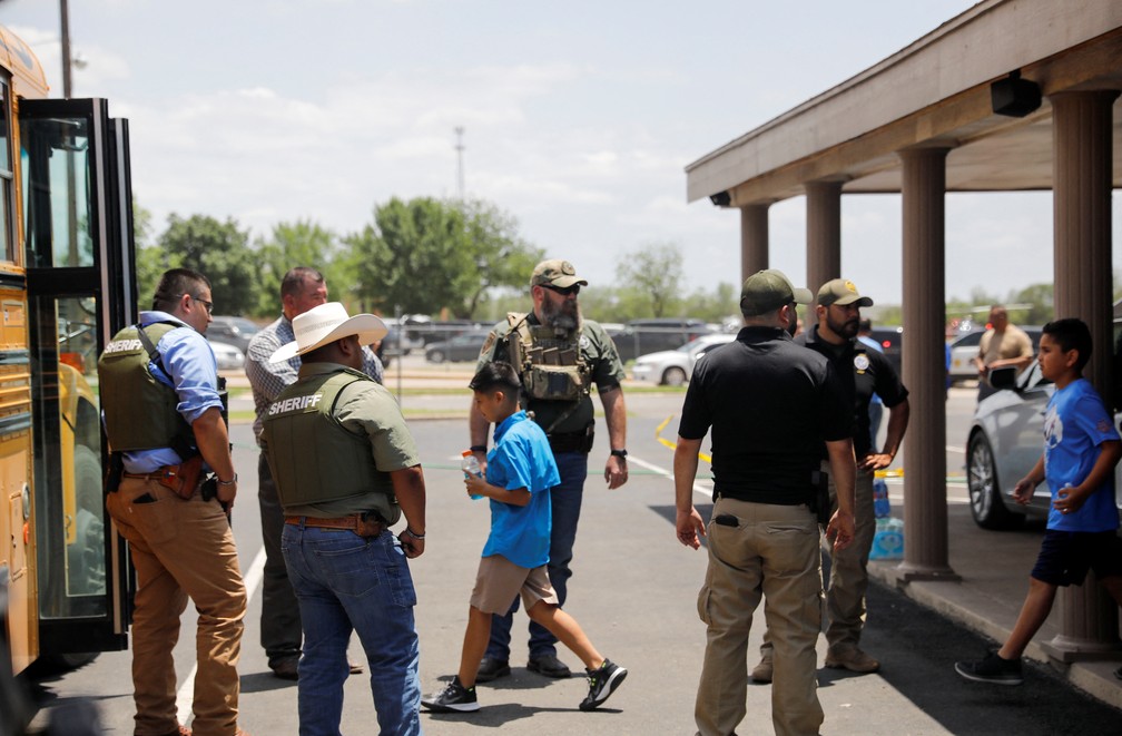 Crianças entram em um ônibus escolar enquanto policiais guardam a cena de um tiroteio suspeito perto da Robb Elementary School em Uvalde, Texas, EUA, em 24 de maio de 2022 — Foto: REUTERS/Marco Bello