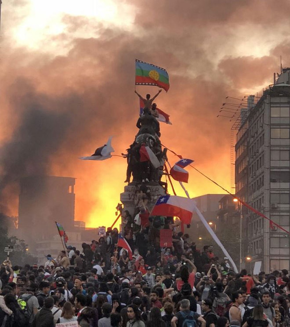 Imagem de manifestante com bandeira Mapuche no topo de estátua militar em Santiago se tornou símbolo dos protestos no Chile por reformas sociais — Foto: Susana Hidalgo/BBC