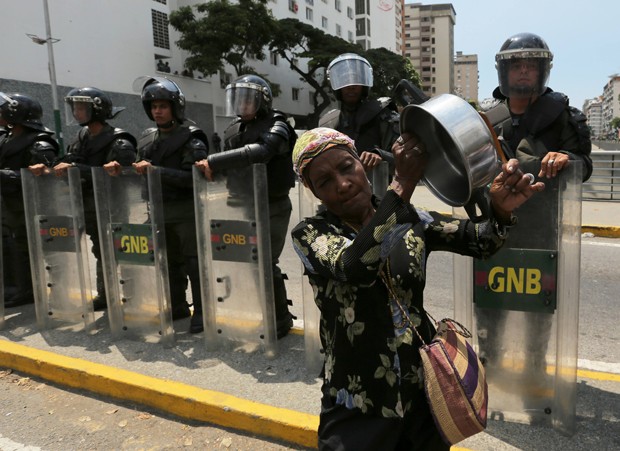 Mulher bate em panela vazia diante de membros da Guarda Nacional Bolivariana durante protesto em Caracas, na Venezuela (Foto: Fernando Llano/AP)