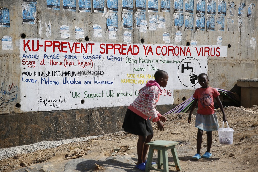 2 de abril - Duas meninas vendem amendoim em frente a um mural informativo, em Nairóbi, Quênia — Foto: Brian Inganga/AP