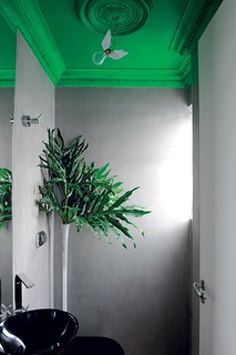 Este lavabo com paredes cinza teve o teto pintado com tinta neon spray. A técnica usada pelo designer de interiores Gustavo Jansen foi a seguinte: espirrar todo o conteúdo da lata em um balde e utilizar um rolo. Para arrematar, a luminária com asas de Ingo Maurer