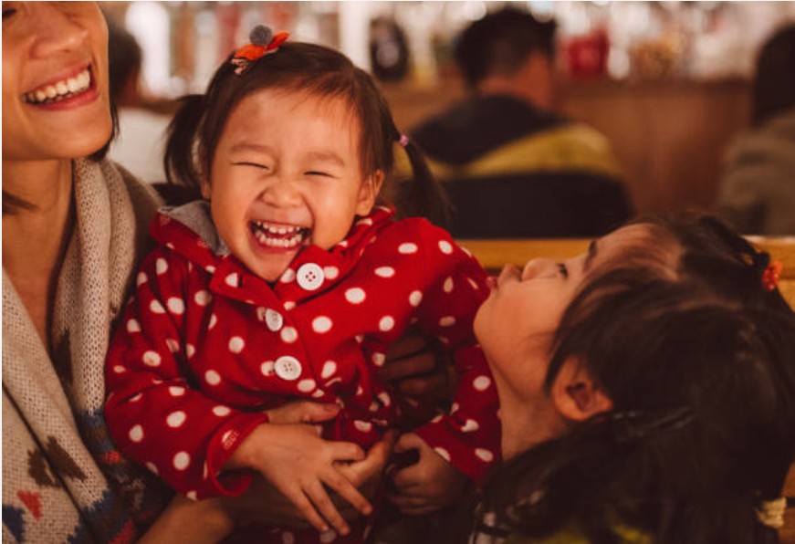 Menina sorrindo em brincadeira com mãe e irmã (Foto: Getty Images)