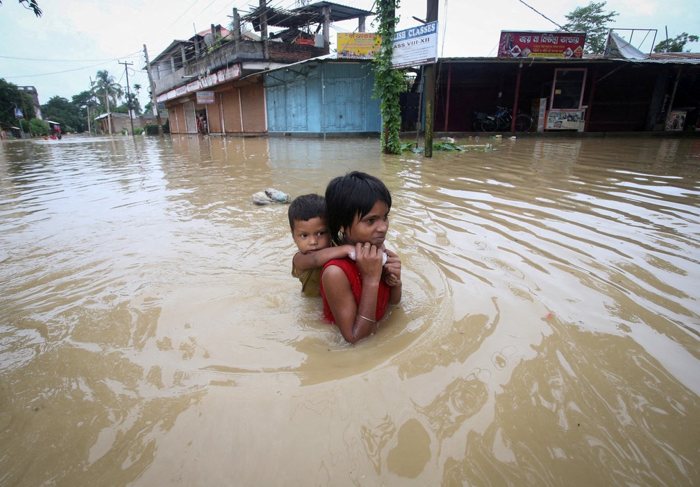 Uma menina carrega seu irmão enquanto caminha por uma estrada inundada nos arredores de Agartala, na Índia. — Foto: REUTERS/Jayanta Dey
