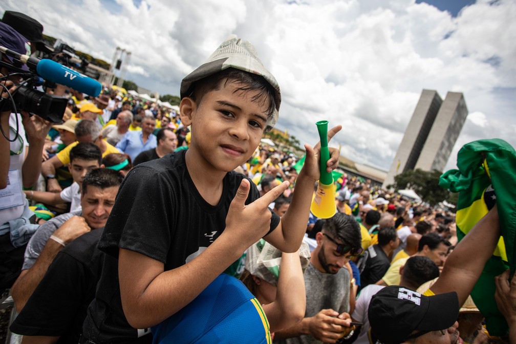 Menino posa para foto fazendo armas com as mãos sobre os ombros de um familiar na Praça dos Três Poderes — Foto: Fábio Tito/G1