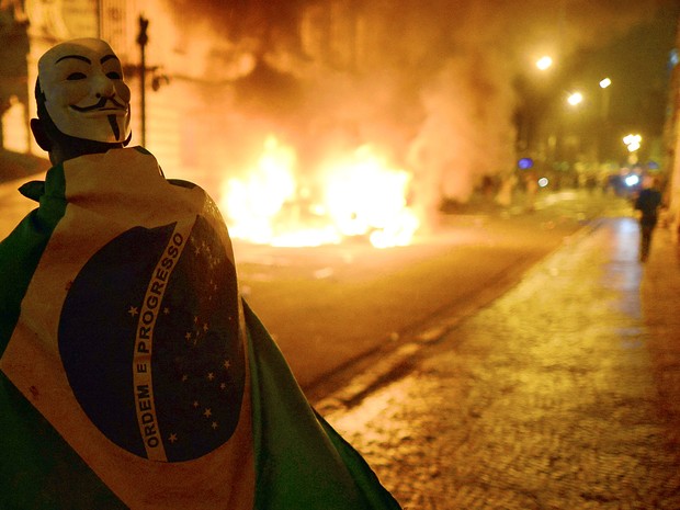 Manifestante mascarado e enrolado em bandeira do Brasil participa de protesto no Centro do Rio (Foto:  Christophe Simon/AFP)