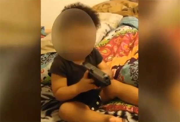 Menina de 1 anos segura arma enquanto pais a ensinam a imitar o som de disparos (Foto: Reprodução / Youtube)