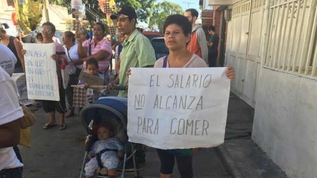 Venezuelanos protestam por conta da pobreza no país com cartazes dizendo que o salário não lhes permite comer e que não há luz, água e/ou gás  (Foto: Guillermo Olmo / BBC Mundo/via BBC News Brasil)