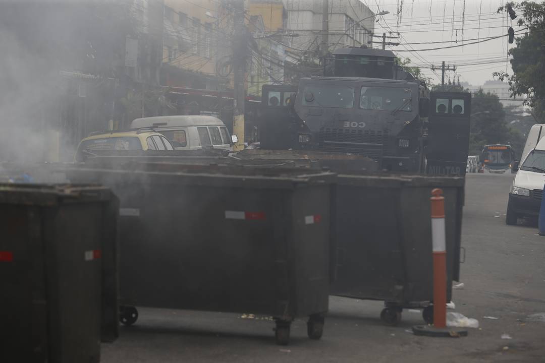 Um blindado da polícia passar em frente a uma barricada incendiada no Complexo da Penha