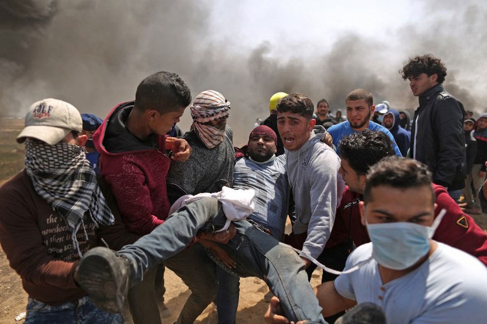 Palestino ferido Ã© carregado apÃ³s confronto com soldados israelenses na fronteira da Faixa de Gaza com o territÃ³rio israelense  (Foto: Mahmud Hams / AFP)