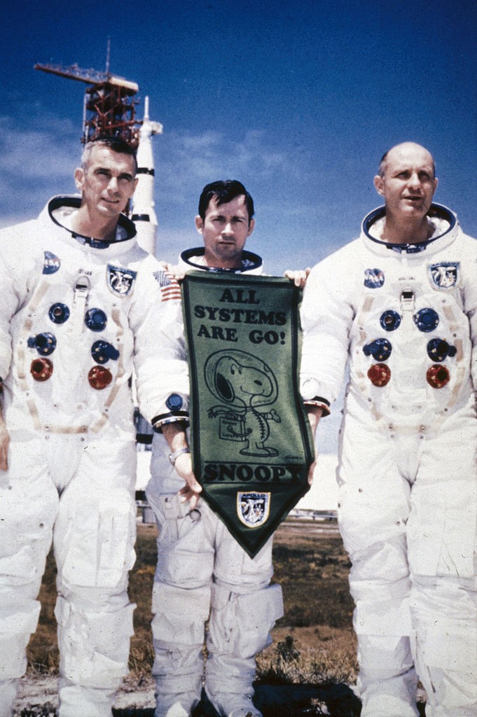 UNITED STATES - JUNE 25:  Left to right; Eugene Cernan, John Young and Thomas Stafford standing in spacesuits in front of the Saturn V rocket carried the Apollo 10 spacecraft. Young is holding a pennant with the legend ?All Systems Are Go!? and a cartoon  (Foto: SSPL via Getty Images)