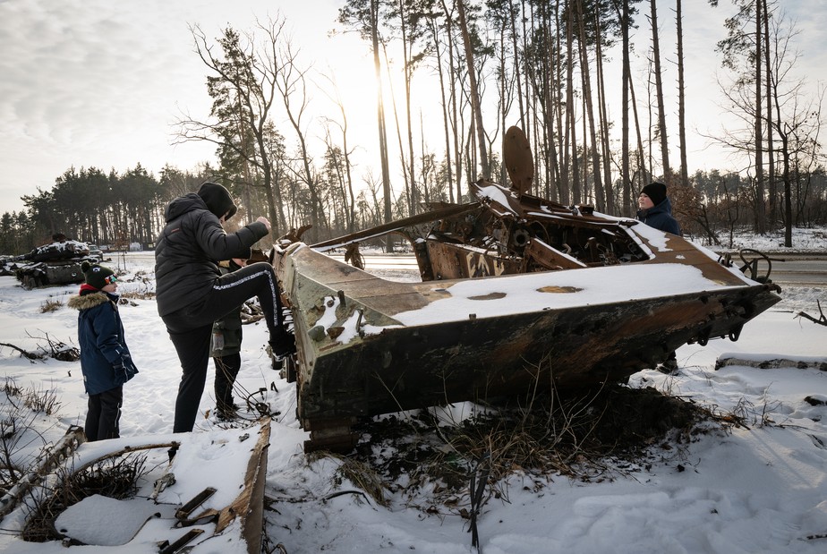 Jovens de Irpin, próximo a Soledar, chutam veículo militar russo destruído, agora coberto de neve, na Ucrânia