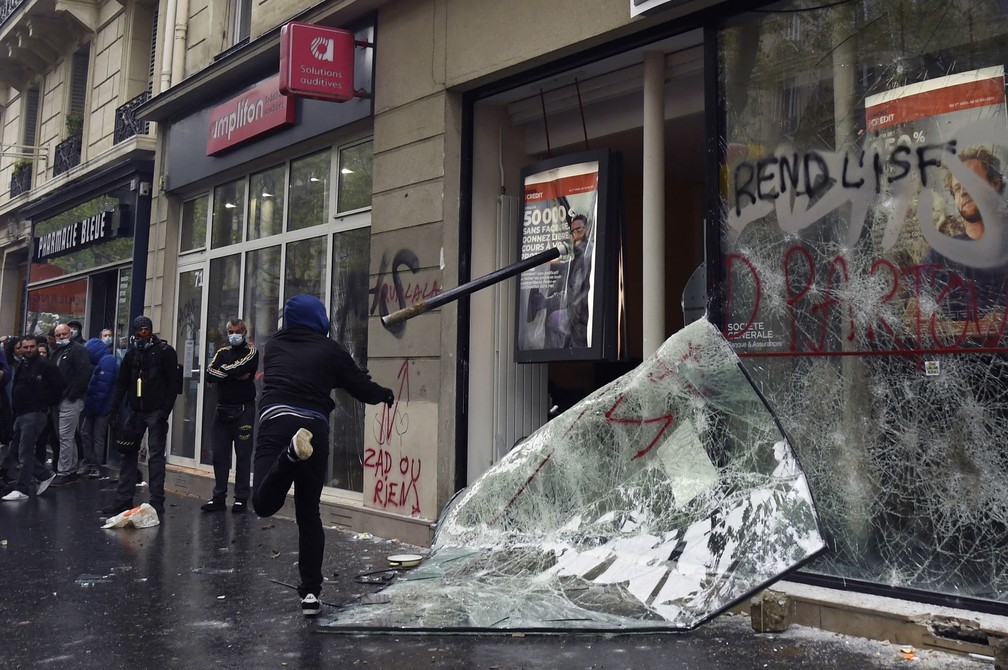 Manifestante atira uma barra contra a janela de um banco durante protesto do Dia do Trabalho, em Paris  — Foto: Bertrand Guay/AFP