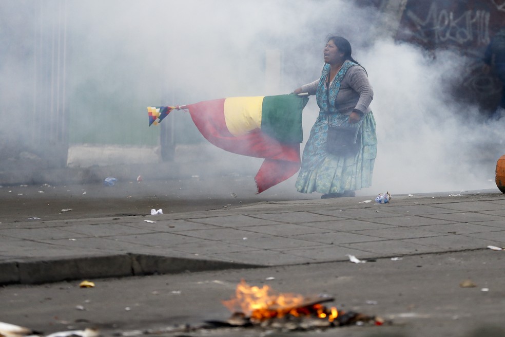 Manifestante com bandeira da Bolívia e Wiphala protesta em La Paz nesta quarta-feira (13) em meio a névoa de gás lacrimogêneo — Foto: Natacha Pisarenko/AP Photo