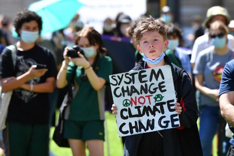 Menino com um cartaz que pede 'mudança no sistema em vez de mudança climática' (Foto: EPA)