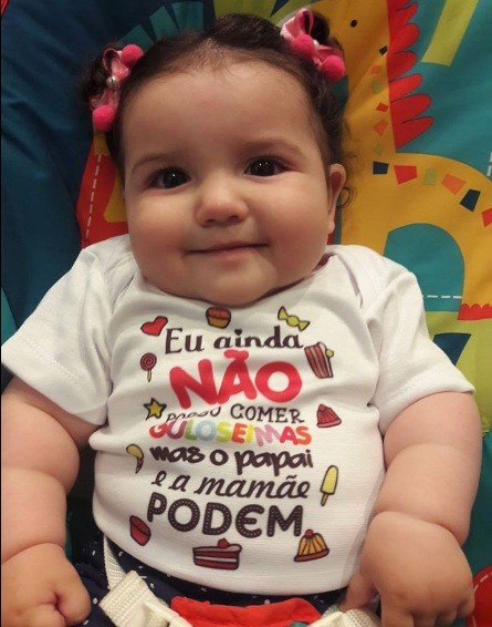 Menina vestindo body com a frase: "Eu ainda não posso comer guloseimas, mas o papai e a mamãe podem” (Foto: Facebook)